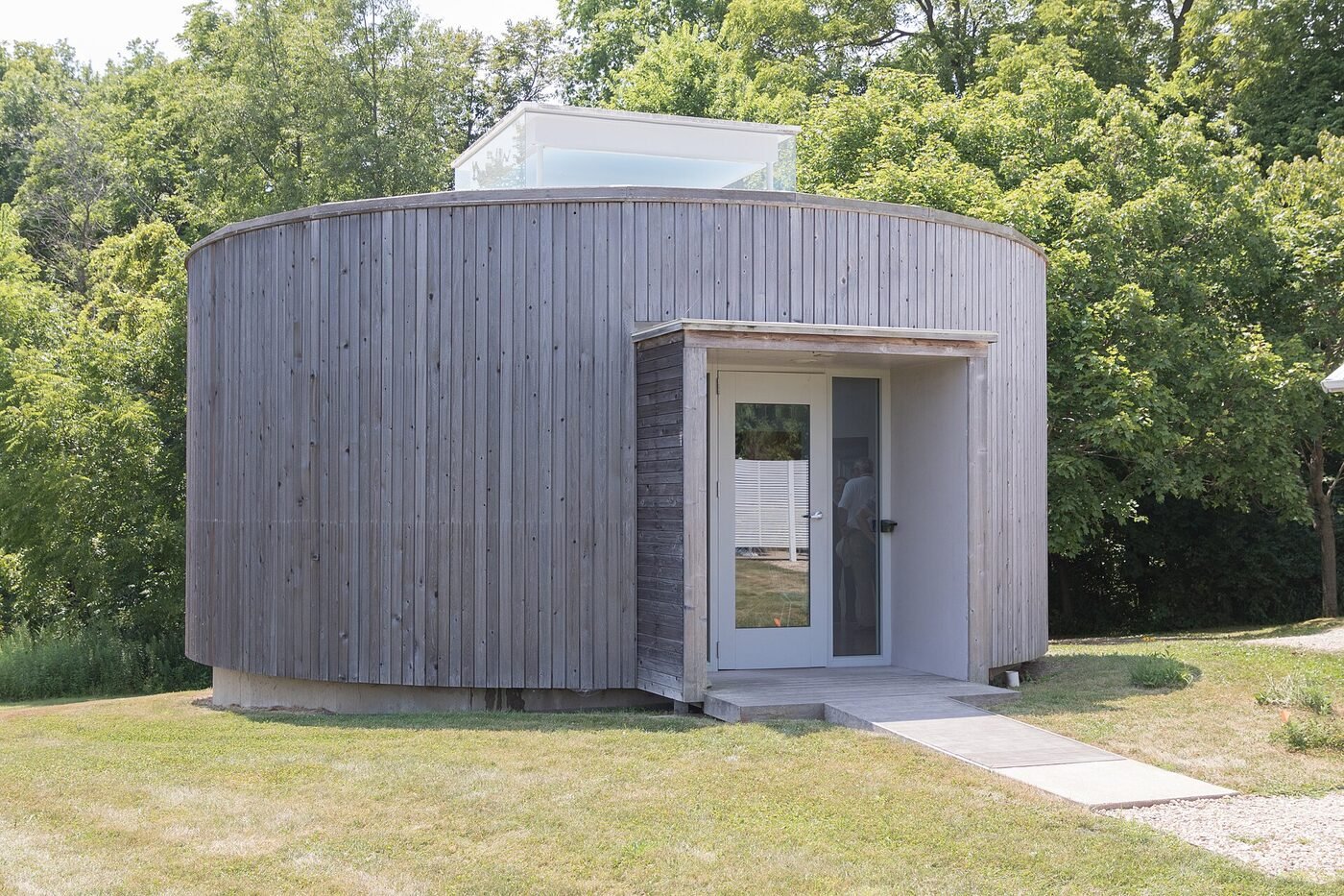 Small timber clad pavilion at the edge of a field